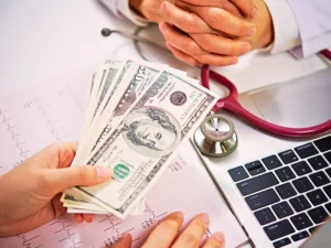 Patient giving money to medical doctor in hospital setting. medical debt and bankruptcy
